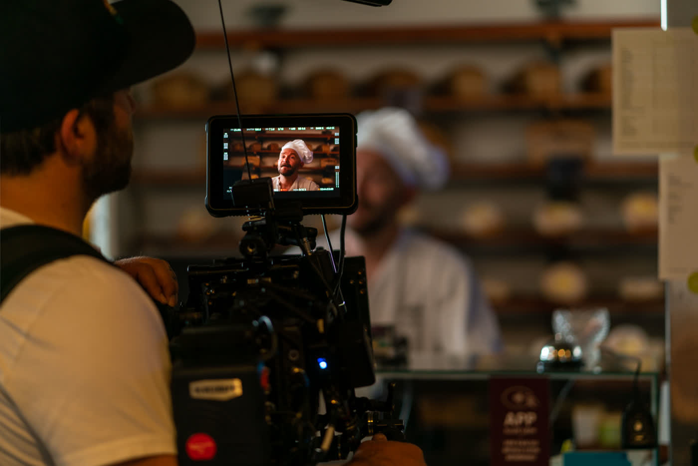 A cinema camera monitor on a real set, a chef out of focus behind it